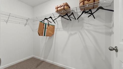 Kennebec Bellamy Model Home Walk in closet off of main bedroom with wire shelving and carpet flooring.