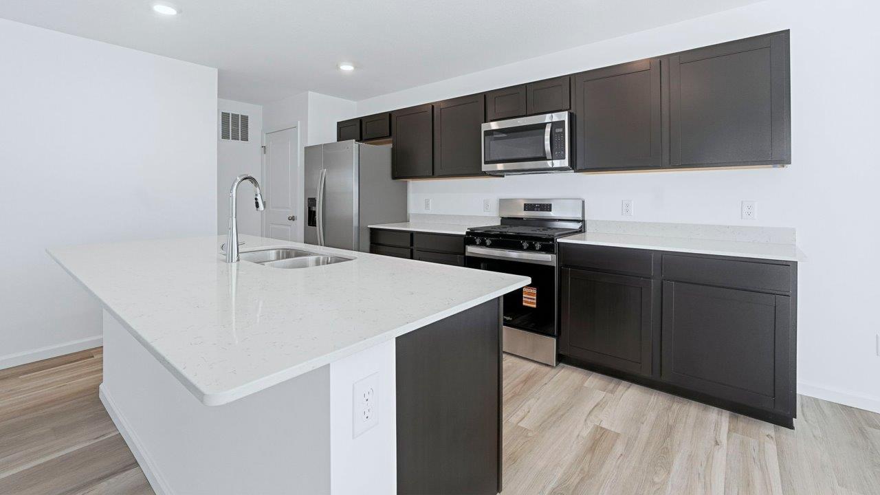kennebec pine kitchen with dark brown cabinets, quartz counters, lvp flooring, center island, and stainless steel appliances