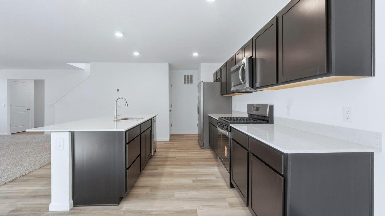 kennebec pine kitchen with dark brown cabinets, quartz counters, lvp flooring, center island, and stainless steel appliances
