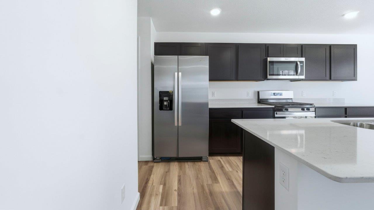kennebec pine kitchen with dark brown cabinets, quartz counters, lvp flooring, center island, and stainless steel appliances