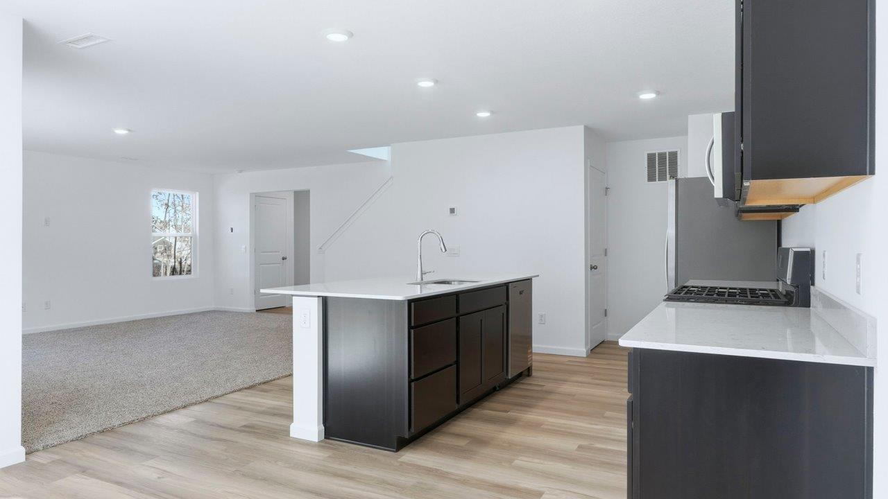 kennebec pine kitchen with dark brown cabinets, quartz counters, lvp flooring, center island, and stainless steel appliances