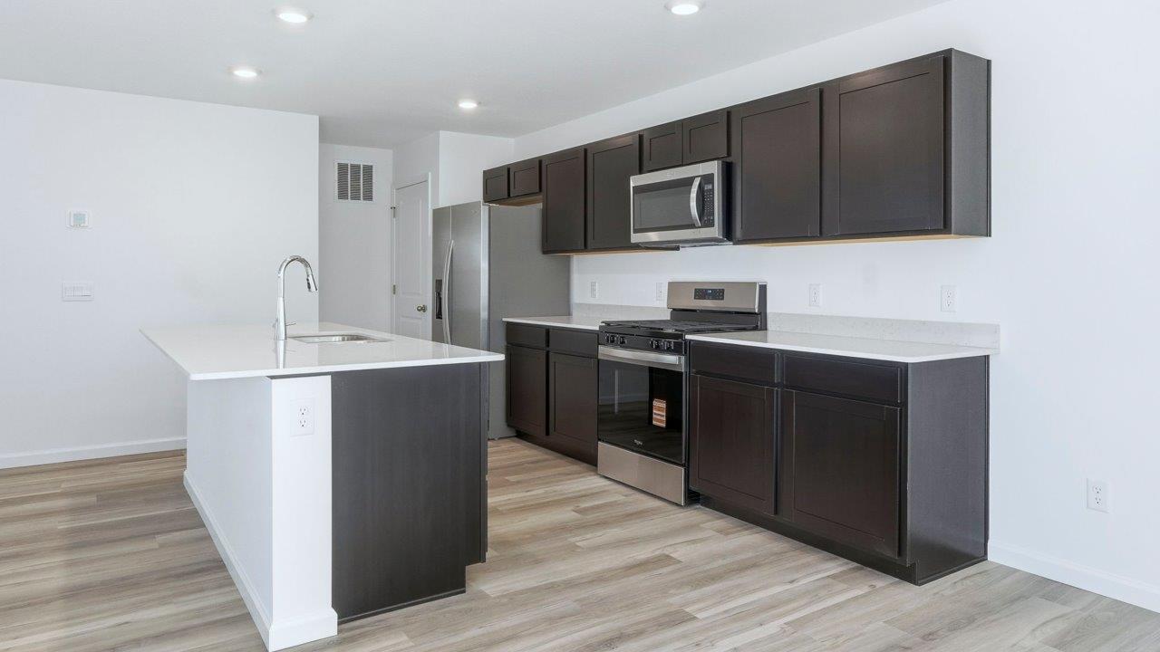 kennebec pine kitchen with dark brown cabinets, quartz counters, lvp flooring, center island, and stainless steel appliances