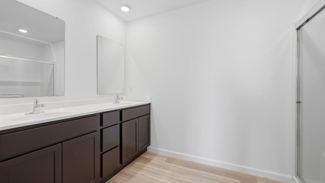 kennebec elm primary ensuite bathroom with dual sink vanity, sarsaparilla cabinetry, private toilet room, linen closet, walk in shower, and mohawk avery lvp flooring