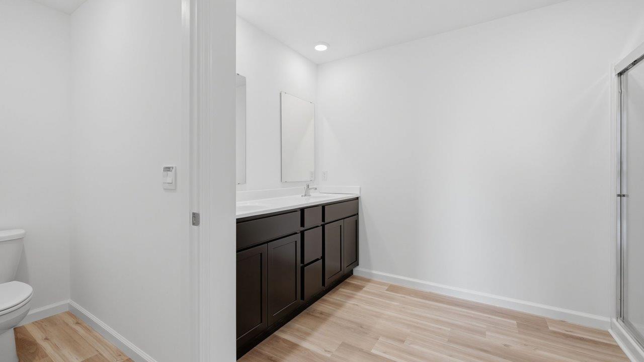 kennebec elm primary ensuite bathroom with dual sink vanity, sarsaparilla cabinetry, private toilet room, linen closet, walk in shower, and mohawk avery lvp flooring