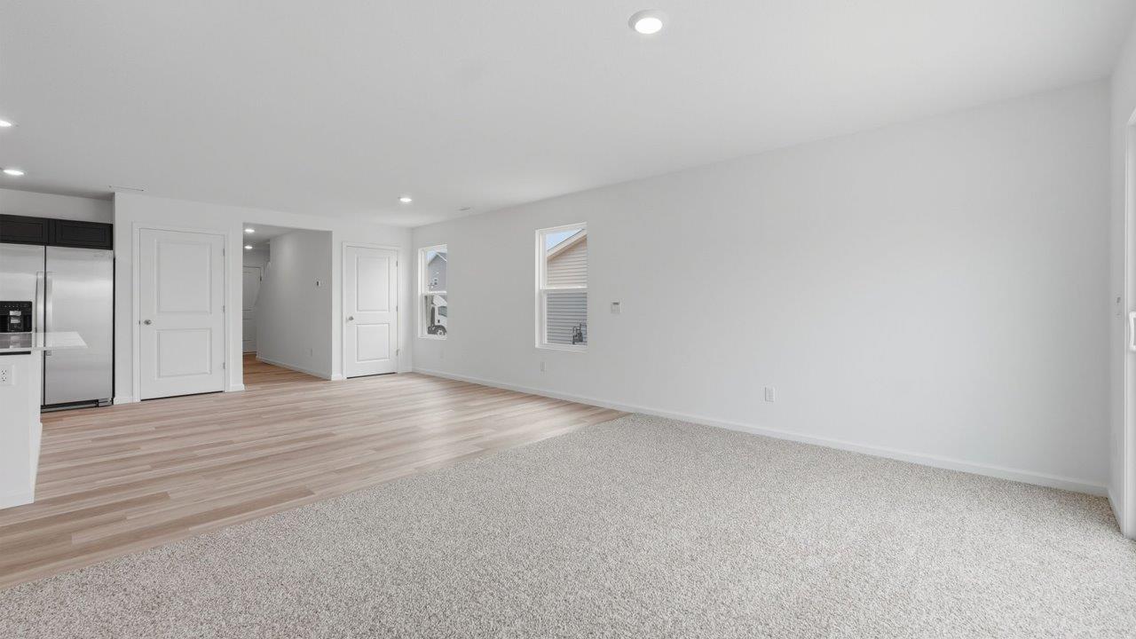 kennebec elm open layout living room with carpet flooring, white walls, and sliding glass door to backyard patio and next to casual dining room with lvp flooring