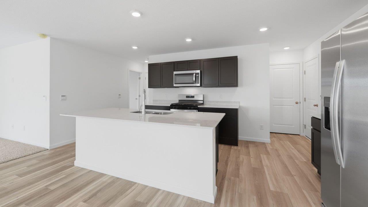 kennebec elm kitchen with sarsaparilla cabinets, stainless steel appliances, quartz countertops, and island with bar seating