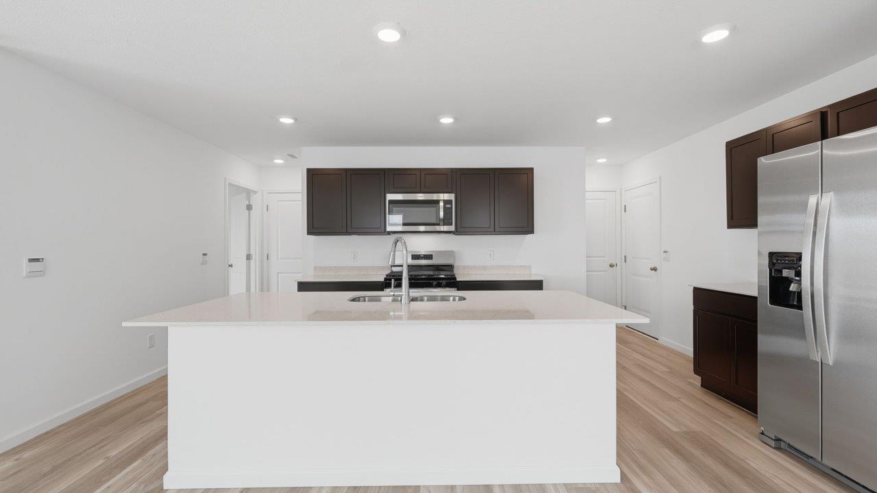 kennebec elm kitchen with sarsaparilla cabinets, stainless steel appliances, quartz countertops, and island with bar seating