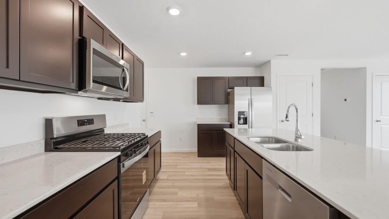 kennebec elm kitchen with sarsaparilla cabinets, stainless steel appliances, quartz countertops, and island with bar seating