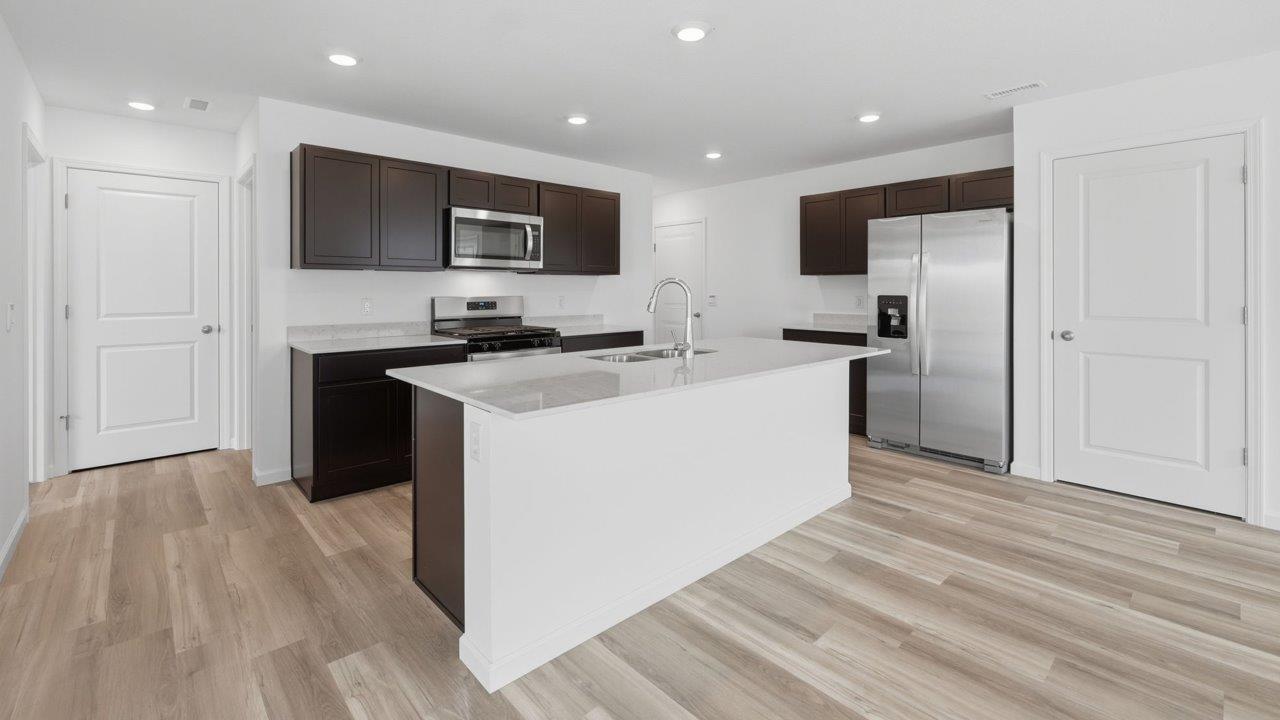 kennebec elm kitchen with sarsaparilla cabinets, stainless steel appliances, quartz countertops, and island with bar seating