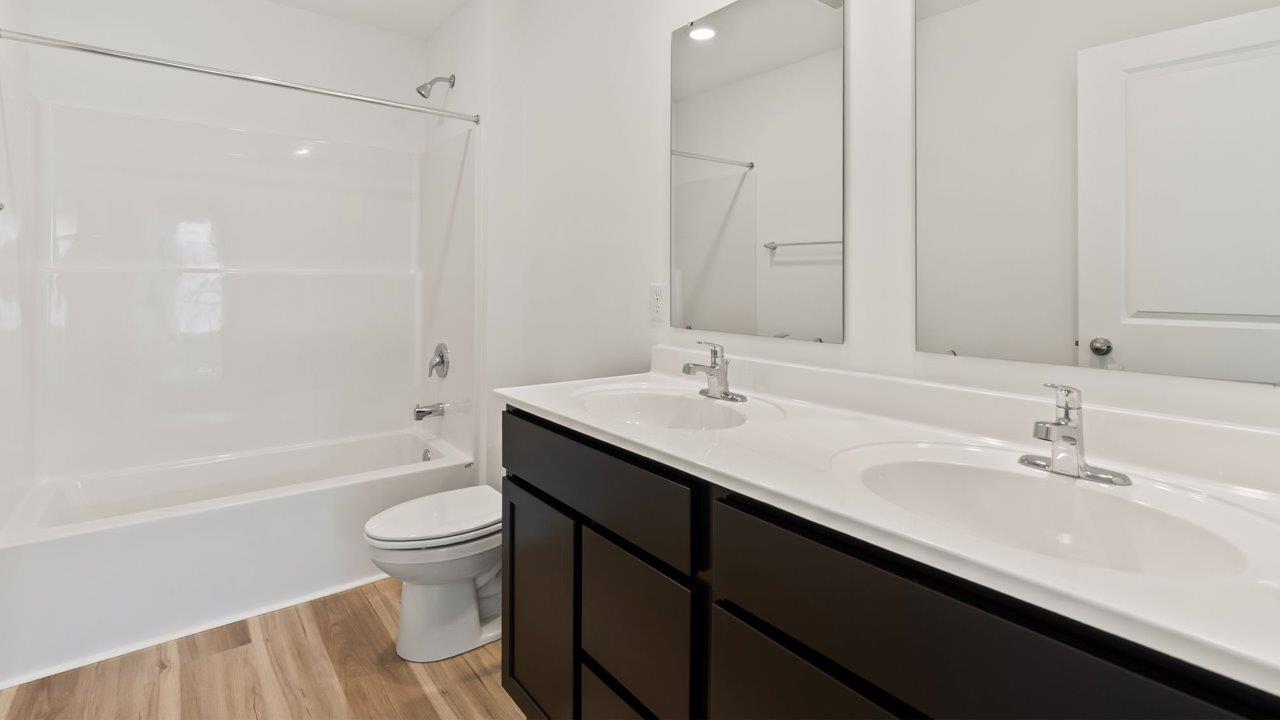 Kennebec Elm C3 - full bathroom with dual vanity sinks with sarsaparilla cabinets, lvp flooring, and fiberglass tub shower