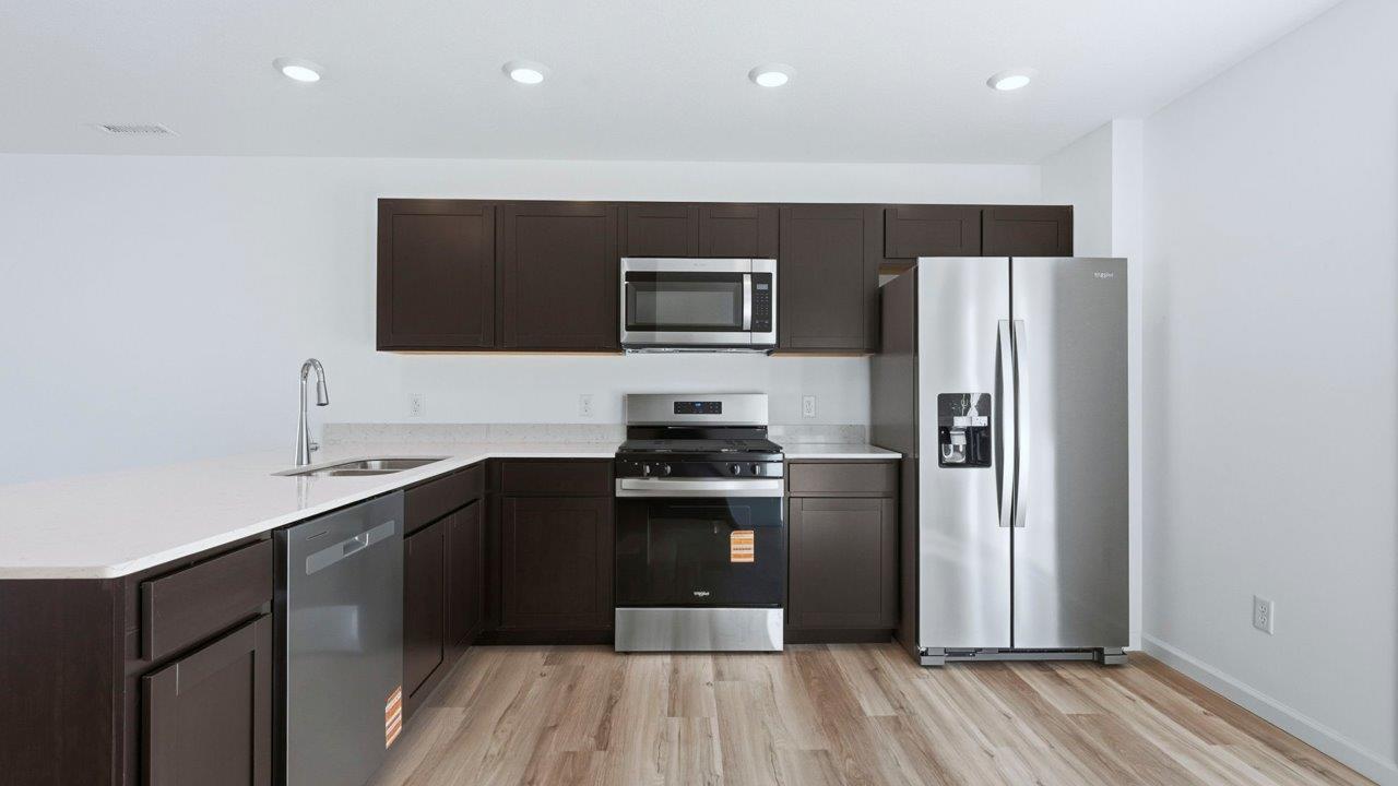 kitchen with sarsaparillla cabinets, quartz counters, lvp flooring, and stainless steel appliances