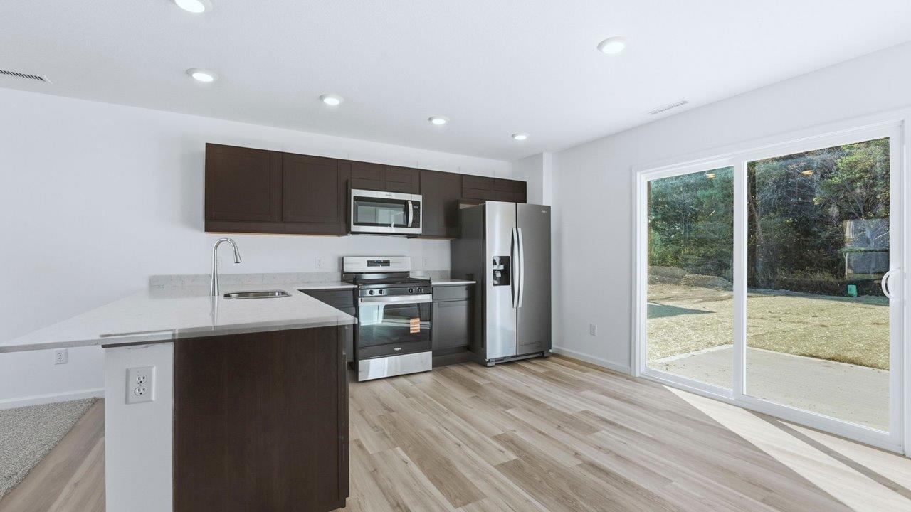 kitchen with sarsaparillla cabinets, quartz counters, lvp flooring, and stainless steel appliances