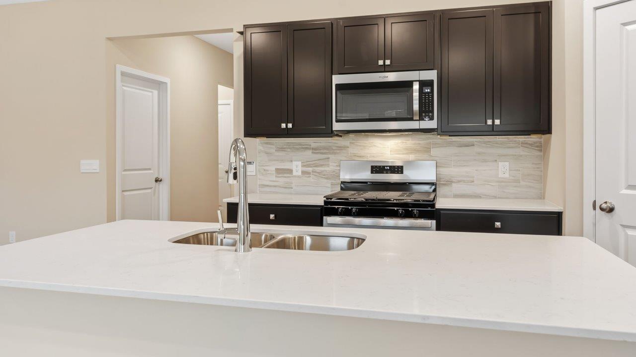 riverwalk villas harmony b3 kitchen with miami vena quartz countertops, sarsaparilla cabints, whirlpool stainless steel appliances, corner pantry, and ceramic tile backsplash