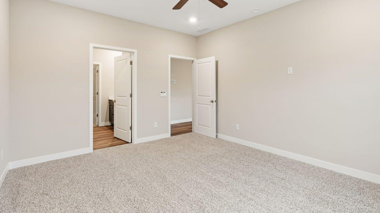 riverwalk villas harmony b3 primary bedroom with elk beige carpet flooring, ceiling fan, 2 windows, and ensuite bathroom and walk in closet