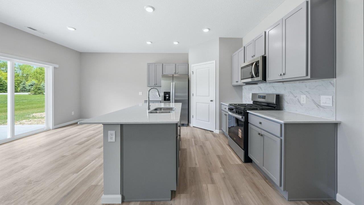 kitchen with gray cabinets, stainless steel appliances, corner pantry, and spacious center island, quartz counters, and ceramic tile backsplash