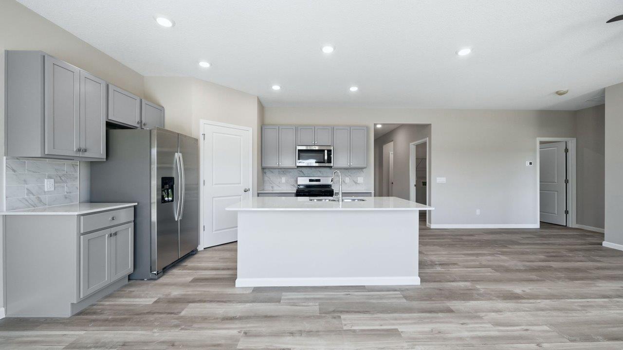 kitchen with gray cabinets, stainless steel appliances, corner pantry, and spacious center island, quartz counters, and ceramic tile backsplash