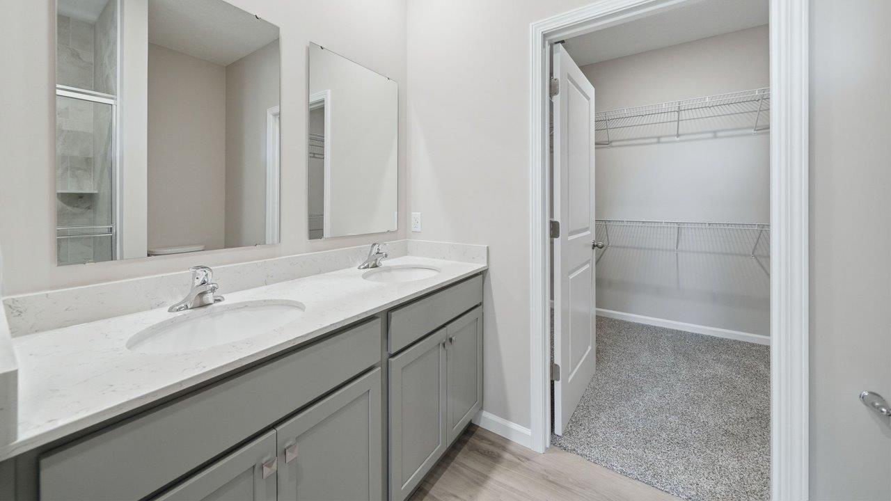 primary bedroom ensuite bathroom with dual sink vanity, ceramic tile shower, and gray cabinets