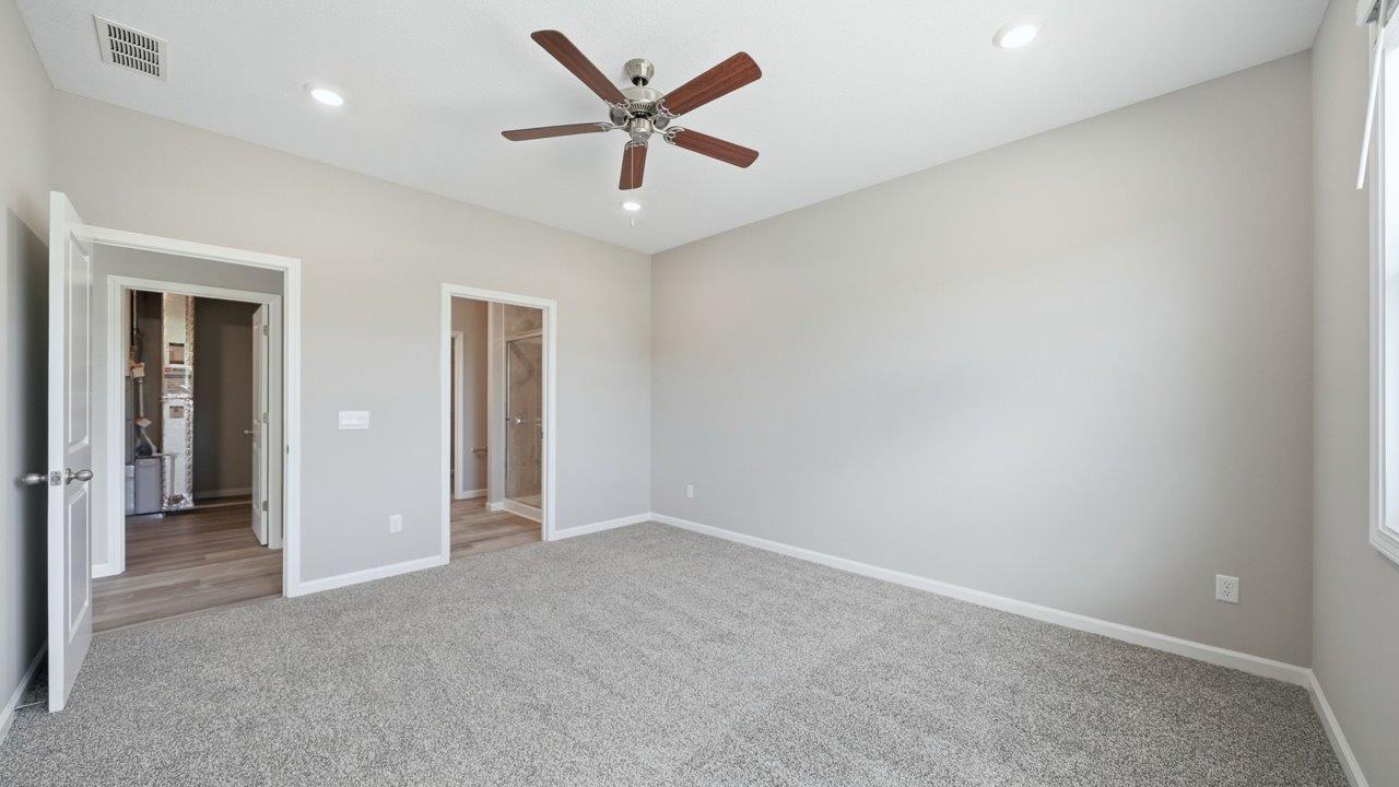 primary bedroom with carpet flooring, ceiling fan, large window, and ensuite walkin closet and bathroom