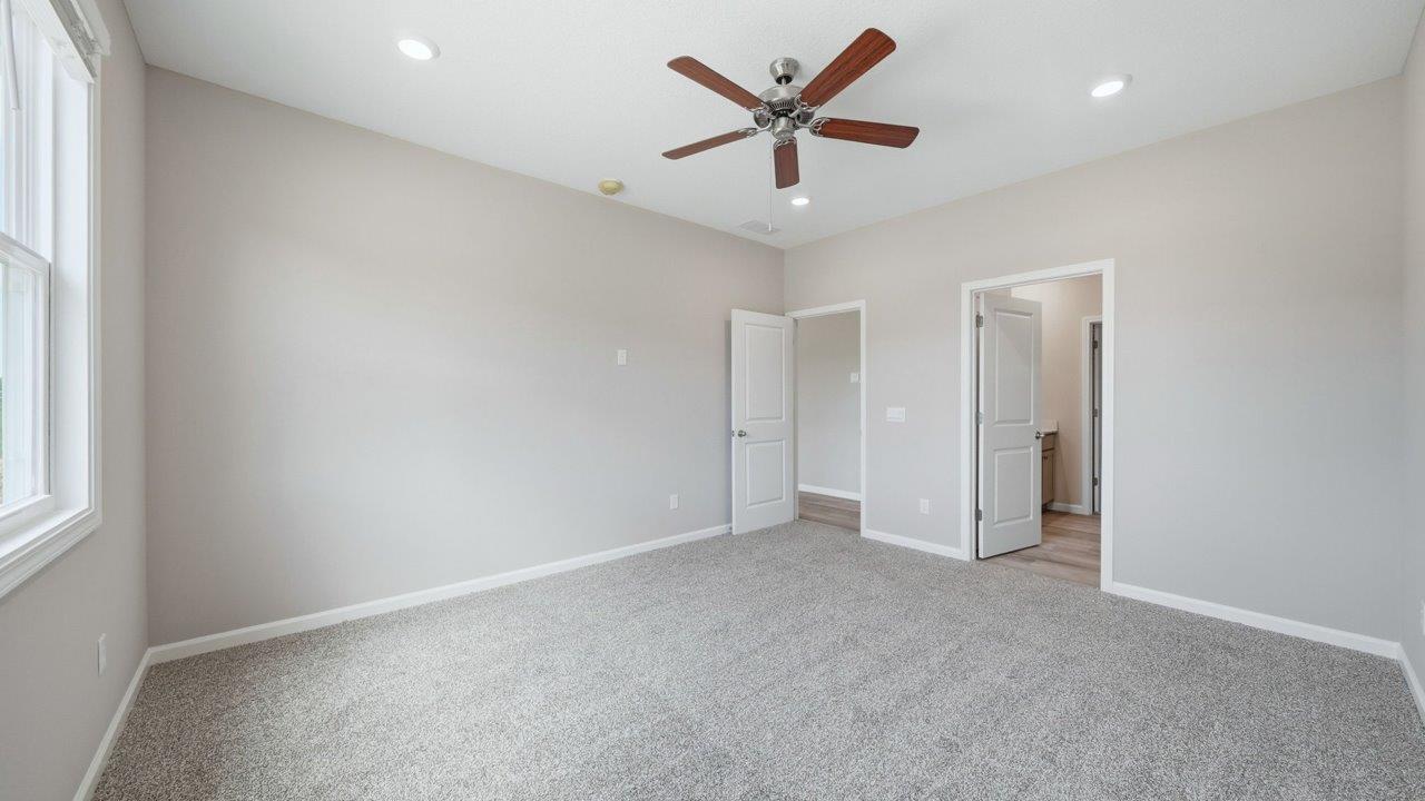 primary bedroom with carpet flooring, ceiling fan, large window, and ensuite walkin closet and bathroom