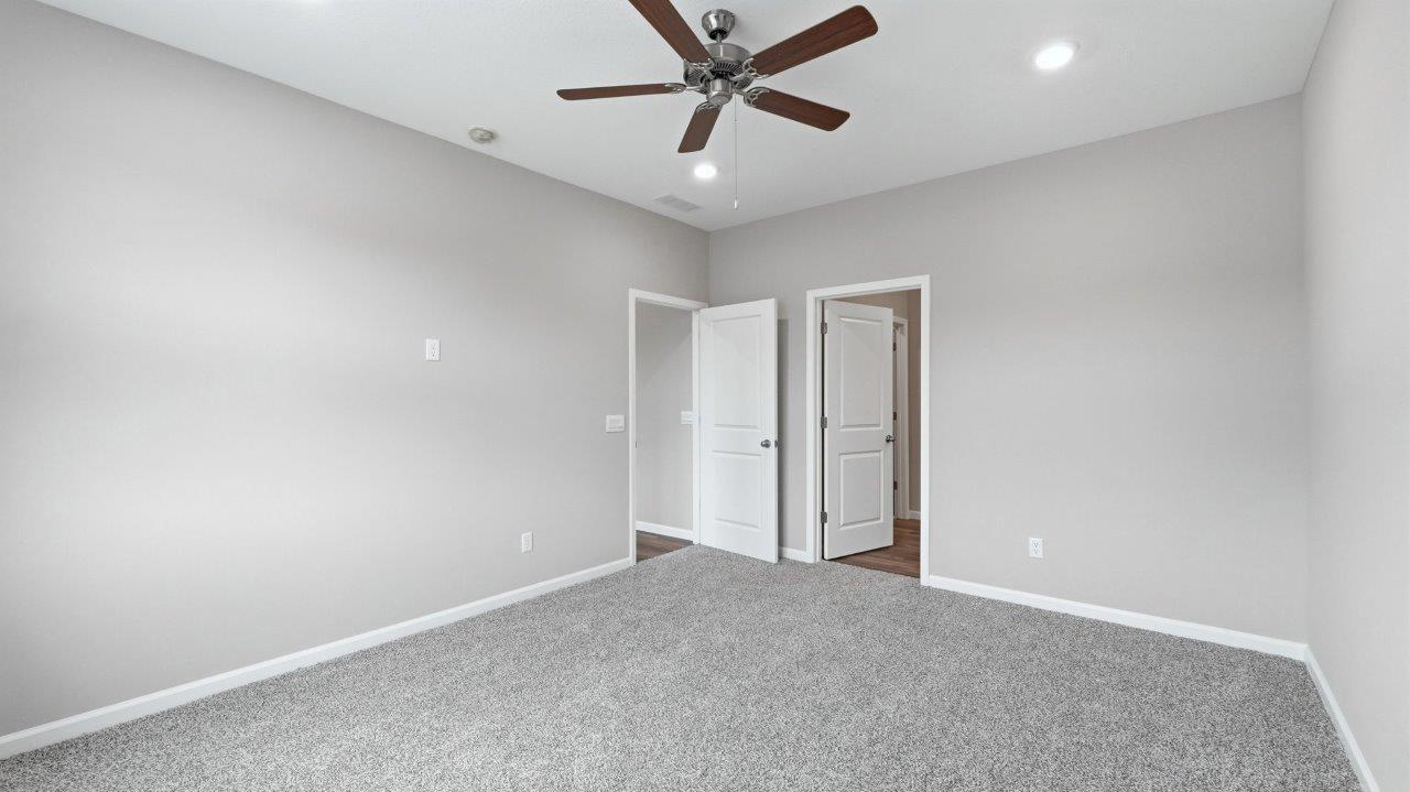 primary bedroom with ensuite bathroom and walk-in closet with carpet flooring, ceiling fan, and 2 windows