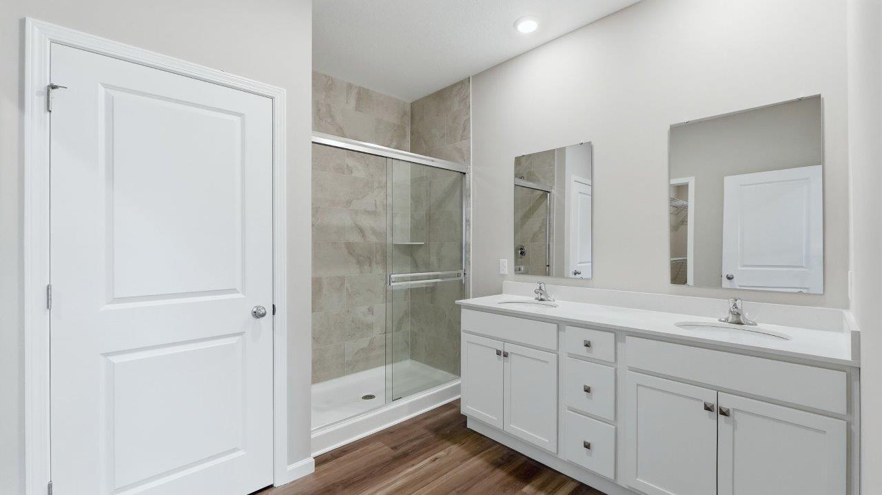 primary ensuite bathroom with dual sink vanity, ceramic tile shower, lvp flooring, and private toilet room