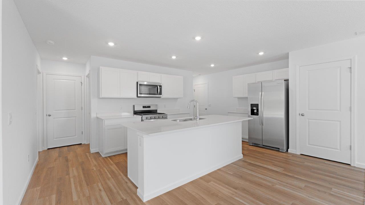elm kitchen with lvp flooring, white cabinets, quartz counters, stainless steel appliances, and center island with bar seating