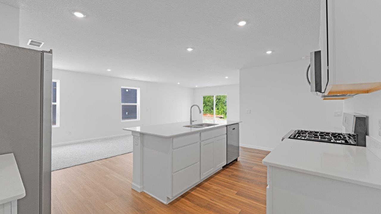 elm kitchen with lvp flooring, white cabinets, quartz counters, stainless steel appliances, and center island with bar seating