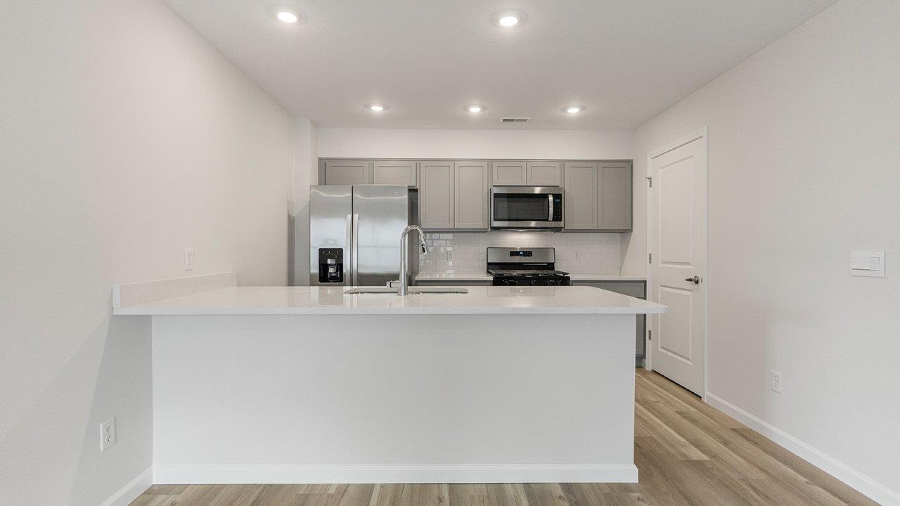 kitchen with grey cabinets, whirlpool stainless steel appliances, white quartz countertops, lvp flooring, and bar seating at island