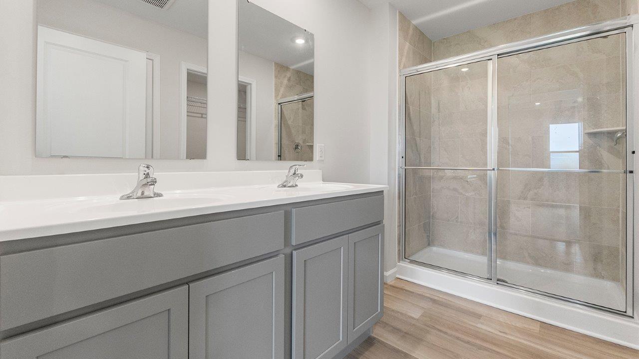 primary ensuite bathroom with dual sink vanity, grey cabinets, white marble counters, lvp flooring, and ceramic tile walk-in shower