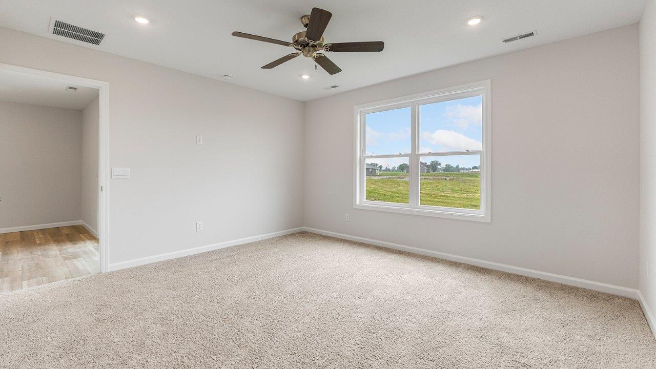 primary bedroom with carpet flooring, 2 windows, fan, and ensuite bath/closet