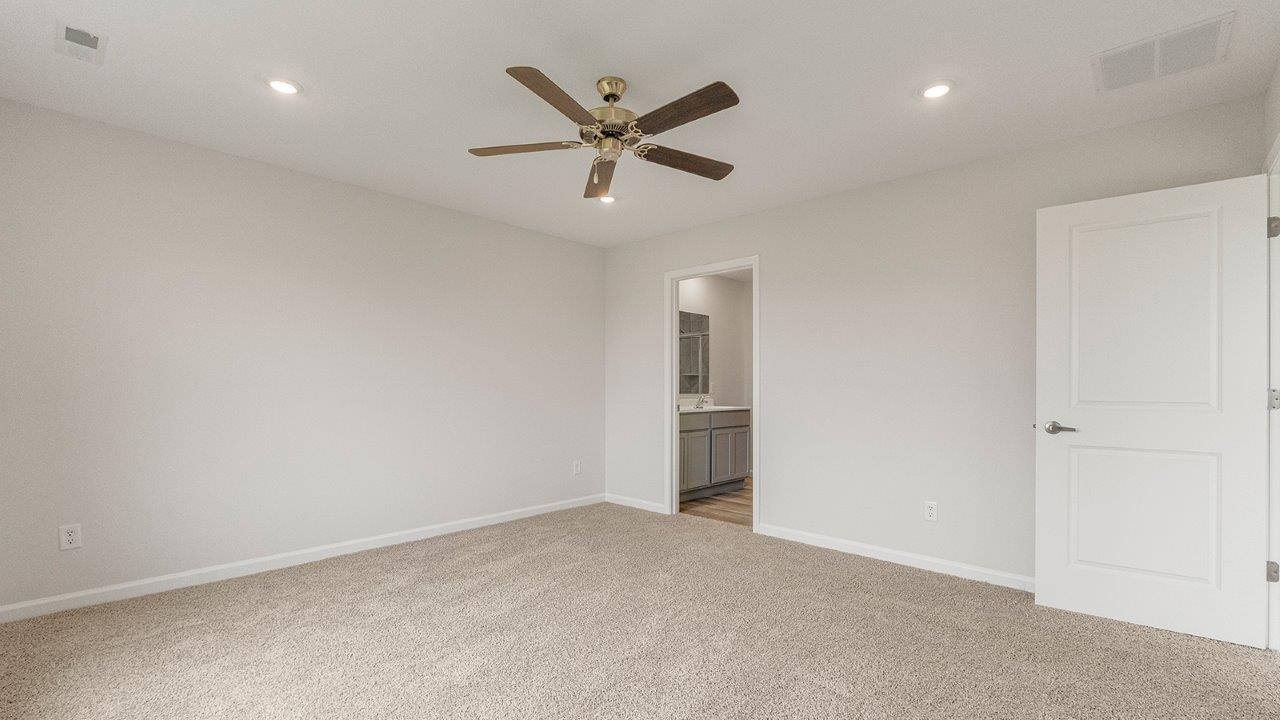 primary bedroom with carpet flooring, 2 windows, fan, and ensuite bath/closet
