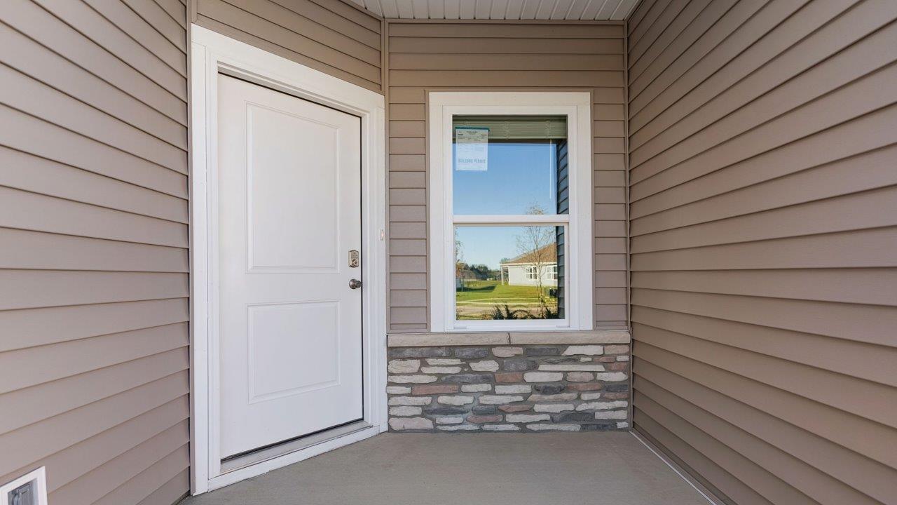 livingston lakes paired villas olsen plan exterior with sodded yard, landscaping, covered front door patio, and stone exterior