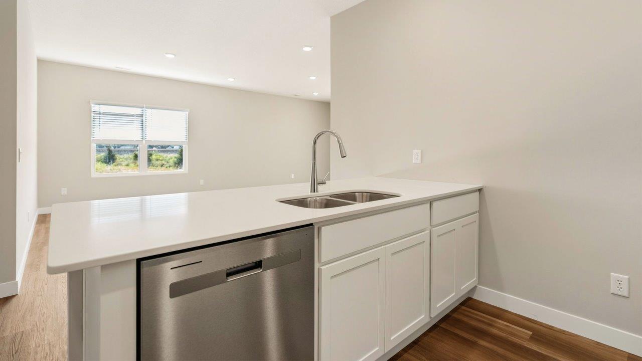 livingston lakes paired villas olsen kitchen penninsula with white cabinets, quartz countertops, stainless steel dishwasher, and sink overlooking living room