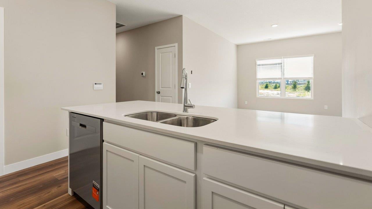 livingston lakes paired villas olsen kitchen penninsula with white cabinets, quartz countertops, stainless steel dishwasher, and sink overlooking living room