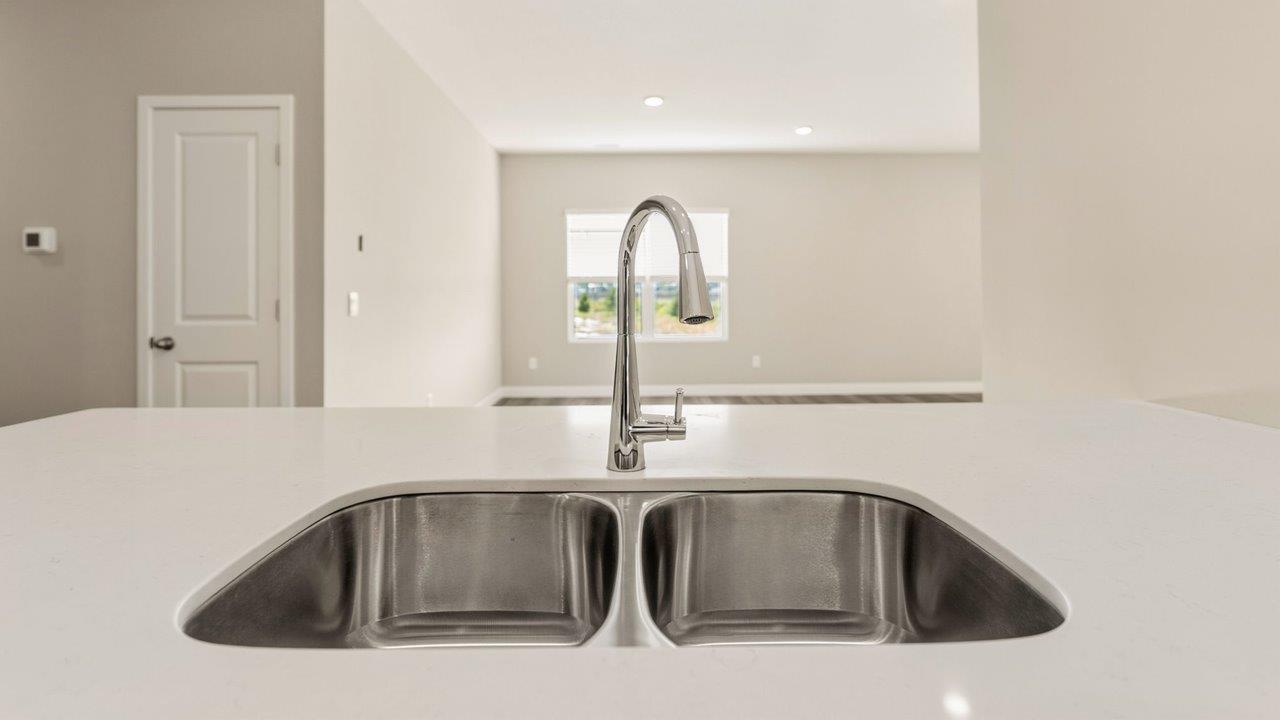 livingston lakes paired villas olsen kitchen penninsula with white cabinets, quartz countertops, stainless steel dishwasher, and sink overlooking living room