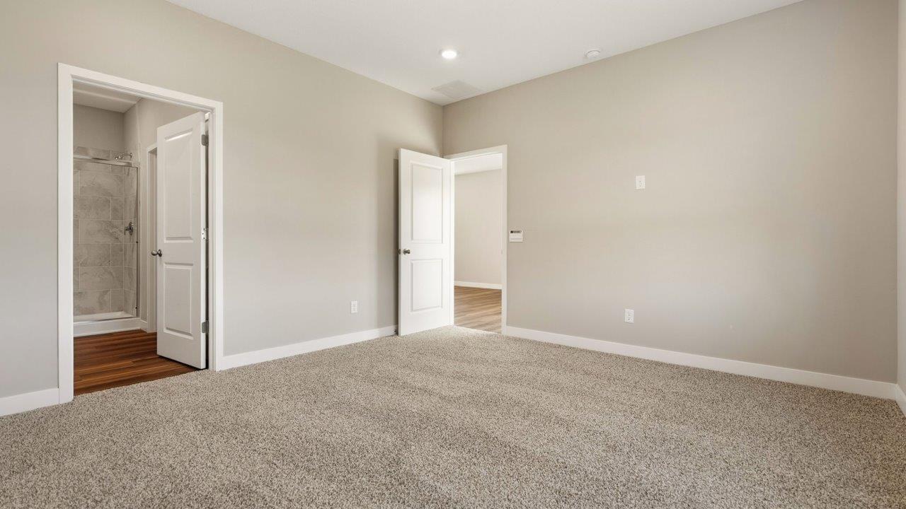livingston lakes paired villas olsen primary bedroom with beige carpet flooring, 2 large windows, and ensuite bathroom and walk in closet