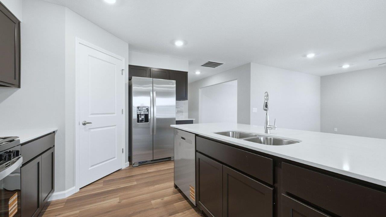 kitchen with mohawk lvp, stainless steel appliances, sarsaparilla shaker cabinets, quartz countertops, corner pantry, and center island with bar seating