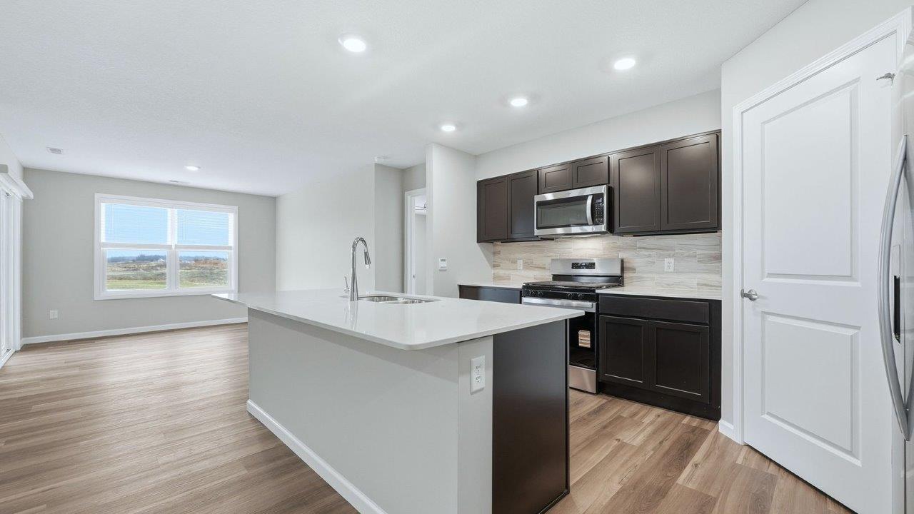 kitchen with mohawk lvp, stainless steel appliances, sarsaparilla shaker cabinets, quartz countertops, corner pantry, and center island with bar seating