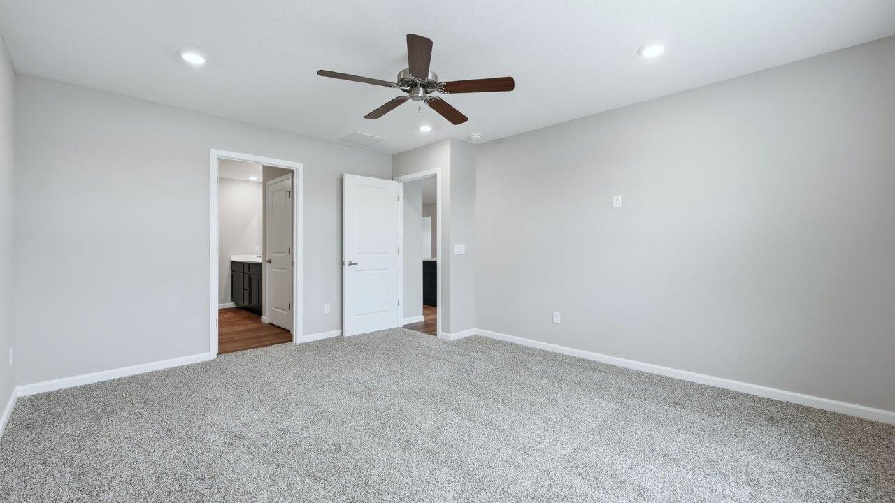 primary bedroom with beige carpet, popular grey walls, ceiling fan, and ensuite bathroom and walk-in closet
