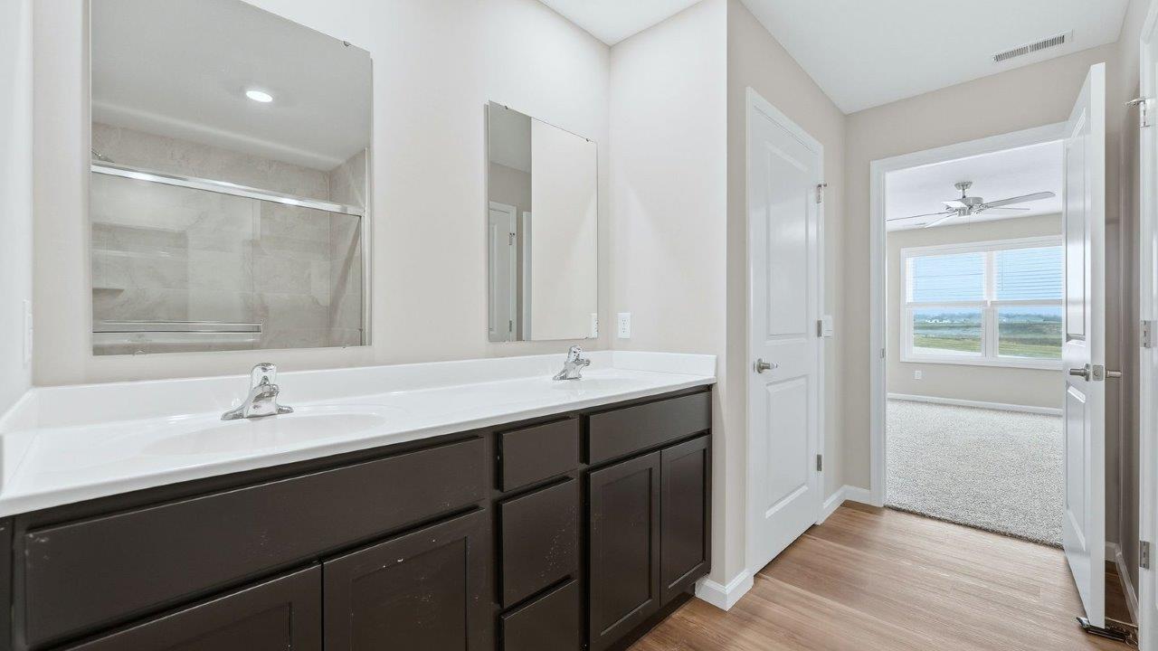 primary ensuite bathroom with dual vanity sinks, quartz counters, sarsaparilla cabinets, lvp flooring, private water room, and walk-in ceramic tile shower