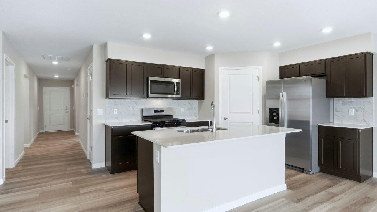 kitchen with sarsaparilla cabinets, island, quartz counters, stainless steel appliances, backsplash, and corner pantry