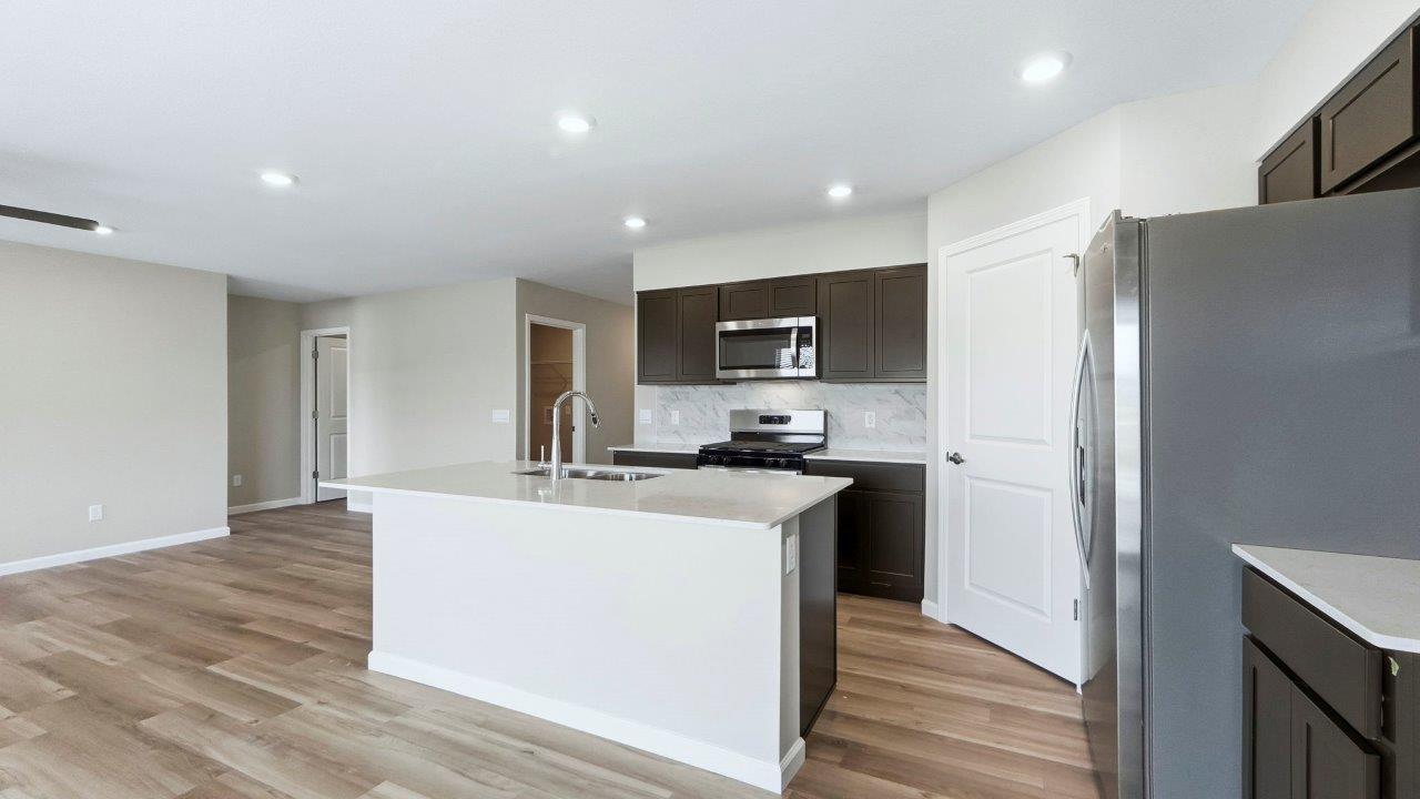 kitchen with sarsaparilla cabinets, island, quartz counters, stainless steel appliances, backsplash, and corner pantry