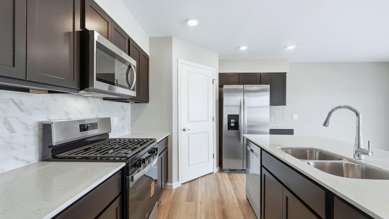 kitchen with sarsaparilla cabinets, island, quartz counters, stainless steel appliances, backsplash, and corner pantry