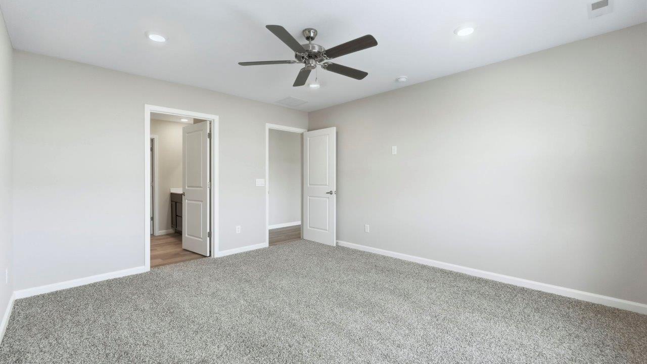 primary bedroom with carpet flooring, 2 windows, ceiling fan, and ensuite bath/closet