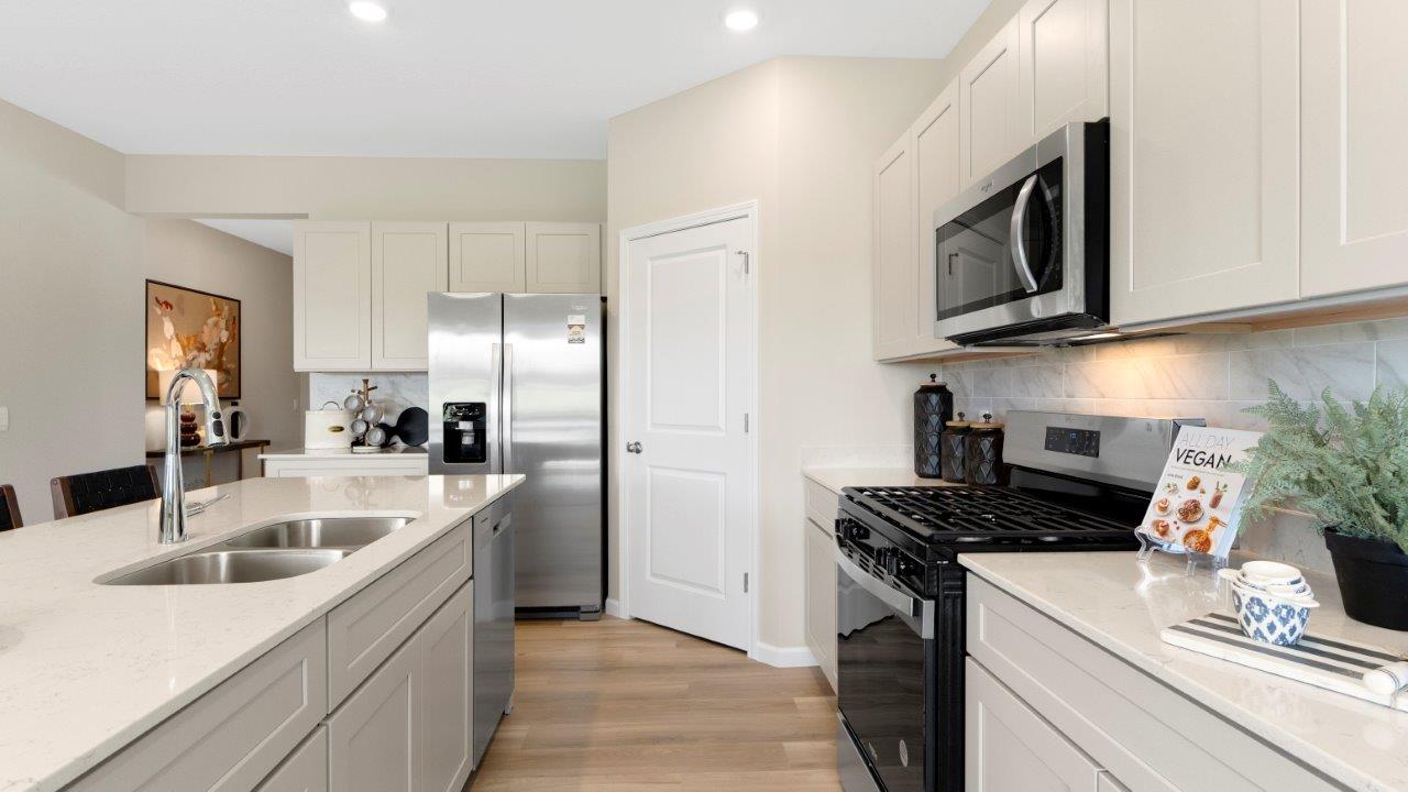 kitchen with white cabinets, quartz countertops, lvp flooring, corner pantry, large center island, and stainless steel appliances