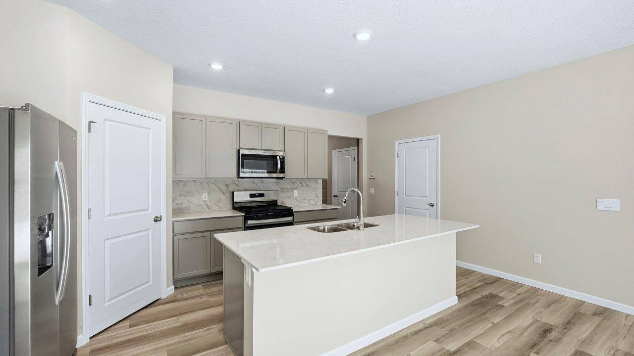 kitchen with grey shaker cabinets, center island, corner pantry, stainless steel appliances, and lyra quartz counters