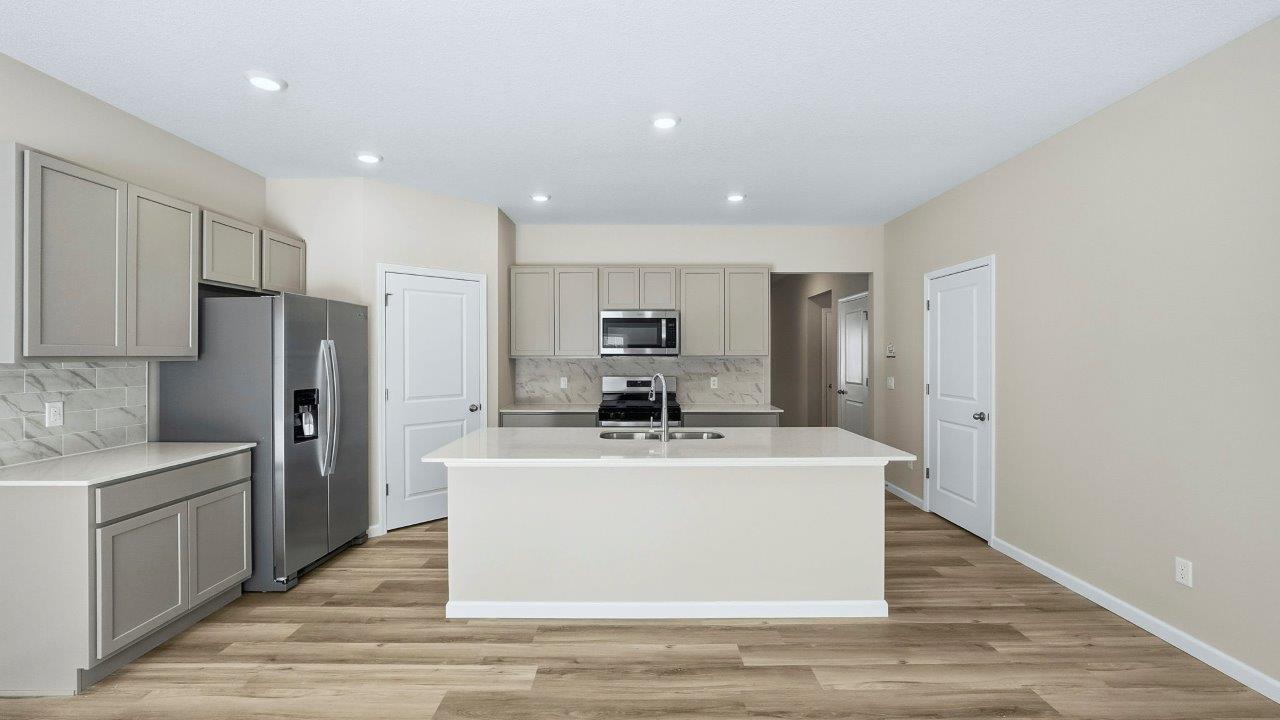 kitchen with grey shaker cabinets, center island, corner pantry, stainless steel appliances, and lyra quartz counters