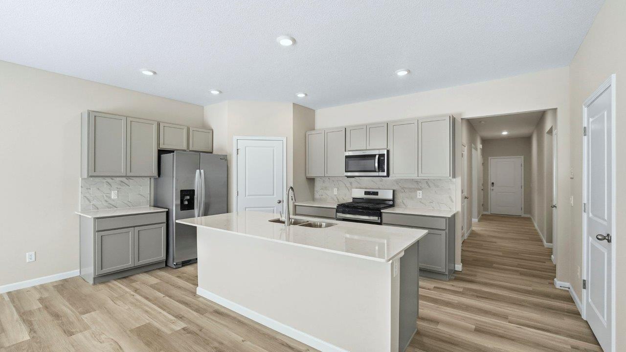 kitchen with grey shaker cabinets, center island, corner pantry, stainless steel appliances, and lyra quartz counters