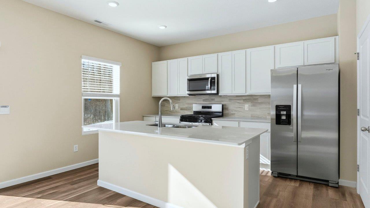 kitchen with white shaker cabinets, Whirlpool stainless steel appliances, quartz countertops, ceramic tile backsplash, and center island with built-in sink, dishwasher, and bar seating