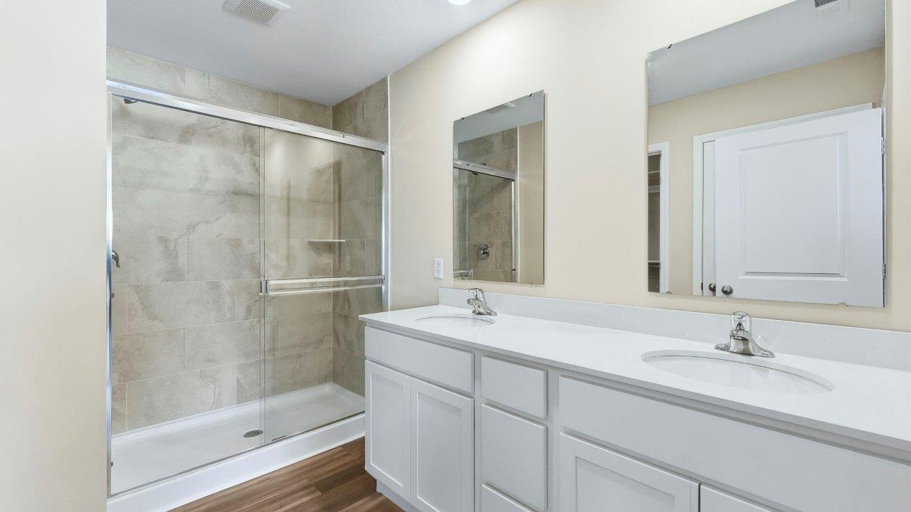 primary ensuite bathroom with dual vanity sinks, white cabinets, quartz counters, private water room, LVP flooring, and ceramic tile walk-in shower
